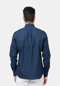 Camicia a maniche lunghe blu navy con colletto, polsini con bottoni e vestibilità rilassata. Tessuto liscio e leggero con dettaglio a piega sul retro.