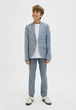 Světlomodrý blazer a odpovídající kalhoty z texturované látky, s dvěma knoflíky, ve spojení s bílým tričkem a černobílými botami.