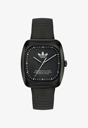Črna kvadratna ura z teksturiranim silikonskim pasom, belimi oznakami ur, srebrnimi kazalci in logotipom Adidas na črnem številčnici.