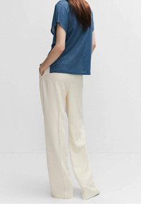 Modrý top s krátkým rukávem a volným střihem v kombinaci s krémovými kalhotami s širokými nohavicemi vyrobenými z lehkého materiálu, s hladkou a jemnou texturou.