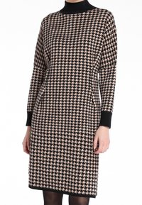 Robe tricotée avec un motif pied-de-poule en noir et beige, col montant, manches longues et poignets côtelés. Texture lisse.