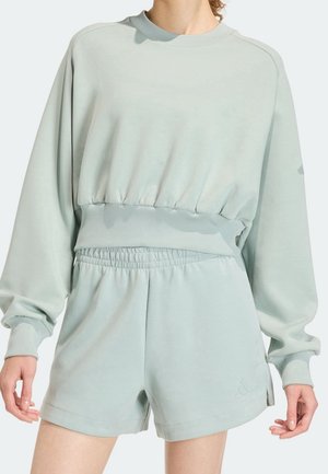 Personne portant un sweat-shirt oversize vert clair avec un ourlet élastique et un short taille haute à taille élastique assorti.