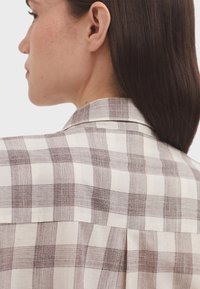 Leichte karierte Hemd in Beige und Braun, mit einem Kragen und Schulterpasse. Der Stoff hat ein strukturiertes, Karo-Muster.