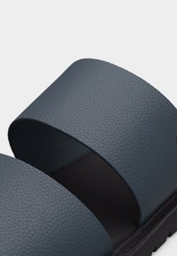 Σκούρο μπλε slide σανδάλι με υφή, δύο φαρδιές λουρίδες και μαύρη σόλα, εμφανίζεται σε κοντινό πλάνο με απλό ανοιχτό φόντο.