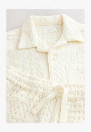 Set od pamučnog kućnog ormara u boji slonove kosti koji uključuje košulju s ovratnikom i gumbima te teksturirane hlače s elastičnim pojasom i vezicama.