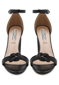 Sandali neri con tacco alto, dotati di un dettaglio a nodo sulla fascia frontale, cinturino alla caviglia con fibbia, punta affilata e superficie in pelle liscia.