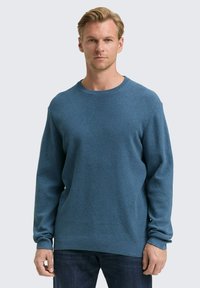 Himmelblaues Strickpullover mit rundem Halsausschnitt, langen Ärmeln und gerippten Bündchen, an einem Modell vor einem neutralen Hintergrund präsentiert.