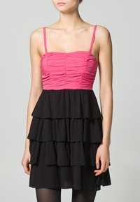 Robe ajustée avec un corsage froncé rose et une jupe noire à volants. Dispose de fines bretelles et d'un ourlet évasé. Texture lisse sur toute la surface.