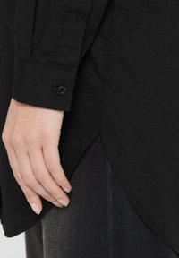 Black long-sleeve shirt with a curved hem and buttoned cuff. Fabric has a smooth texture, featuring a subtle sheen and no visible patterns.