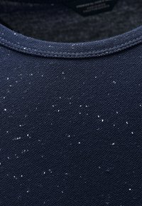 Námořnické modré tričko s texturovanou tkaninou, které má jemný vzor bílých skvrn po celé ploše a kulatý výstřih.