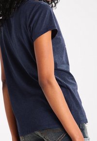 T-paita, jossa on lyhyet hihat, tummansinistä pehmeästä, teksturoidusta kankaasta. Rento istuvuus ja kaareva helma. Näkyvät ompelusaumat hihoissa.