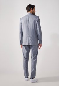 Grau kariertes Anzug mit einer maßgeschneiderten Passform; verfügt über strukturierte Schultern, Reverskragen und schmal zulaufende Hosen. Weiße Sneakers vervollständigen den Look.