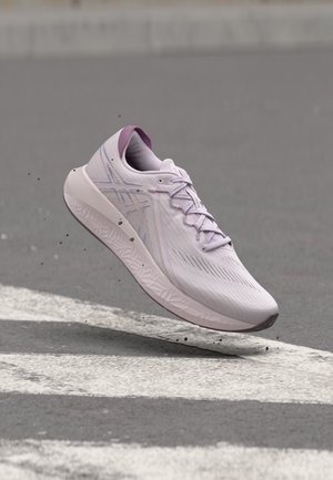 Chaussure de course violet clair avec lacets flottant au-dessus d'une surface pavée avec des marquages routiers blancs et de petits débris en mouvement.
