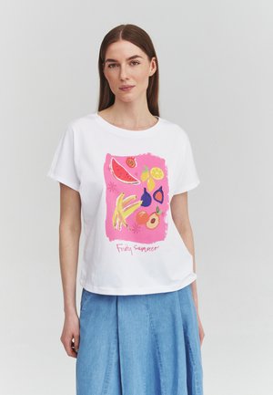 Donna che indossa una maglietta bianca con illustrazione rosa di frutta che include anguria, banana, limone, fico e pesca, abbinata a una gonna azzurra.