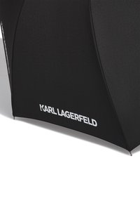 Crni kišobran s teksturiranim krovićem i istaknutim bijelim logotipom "KARL LAGERFELD" sa strane. Ima zakrivljen oblik i špicasti vrh.