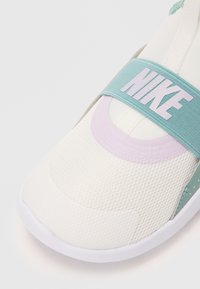 Chaussure Nike avec une tige en mesh gris clair et blanc, une sangle vert menthe arborant un logo blanc, et un accent lavande. Forme de orteil arrondie.