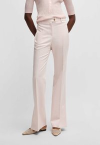Jasnoróżowe cygaretki o prostym kroju, z plisami z przodu i wysokim stanem. W połączeniu z teksturowanymi beżowymi butami.