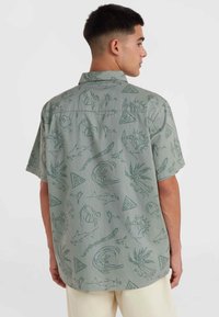 Korte mouwen overhemden van gedempt groene stof met een meerpatroonontwerp dat omtrekken van zeedieren, tribale vormen en abstracte figuren bevat.