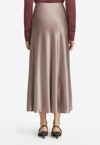 Langer, satinhafter Rock in Mauve, fließende Silhouette, mit glatter Textur und sanftem Glanz. Kombiniert mit einem taillierten Oberteil und hohen Schuhen.