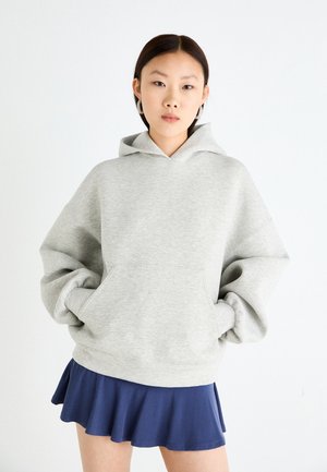 Un sweat à capuche oversize gris clair avec une poche avant, un cordon de serrage sur la capuche et des poignets côtelés, associé à une mini-jupe évasée bleu foncé.