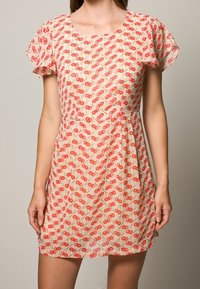 Lyhythihainen, polvipituinen mekko, joka on valmistettu kevyestä, läpikuultavasta kankaasta ja jossa on toistuva kirsikkakuosi punaisena beigeillä taustoilla.