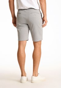 Pantaloni corti grigi in cotone con tasche posteriori con chiusure a bottone, design su misura e taglio al ginocchio, abbinati a sneakers bianche.