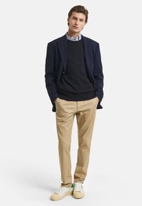 Navy blazer over a black sweater, light blue collared shirt, khaki pants, and white sneakers with green accents. Smooth fabric, tailored fit.