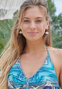Swimsuit with a blue and brown geometric pattern, featuring shoulder straps and gathered fabric at the neckline. Silver earrings visible.