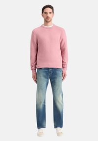 Jersey de punto rosa claro con escote redondo, combinado con jeans rectos azul claro y zapatillas beige. Diseño simple y texturizado.