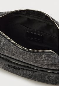 Pochete de tecido cinza com fecho de correr, um forro interior suave e uma etiqueta de logo discreta dentro do bolso. Design estruturado e moderno.