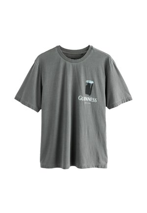 Graues Baumwoll-T-Shirt mit kurzen Ärmeln. Auf der Vorderseite befindet sich ein gedrucktes Guinness-Logo und ein Glas Stout. Mit Rundhalsausschnitt.