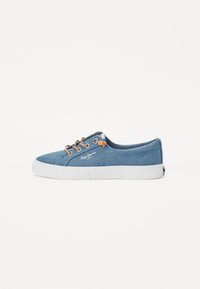 Sapatilha de cano baixo em denim azul com sola de borracha branca. Apresenta atacadores castanhos e detalhes cosidos. Logótipo visível na lateral.