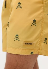 Shorts de baie galbene cu un model repetitiv de oase negre cu craniu, având un etichetă cu logo-ul "SCALPERS" pe lateral. Textură de țesătură netedă.