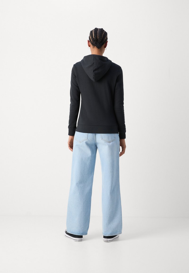 Black hooded sweatshirt with long sleeves, paired with light blue wide-leg jeans and black sneakers, viewed from the back.