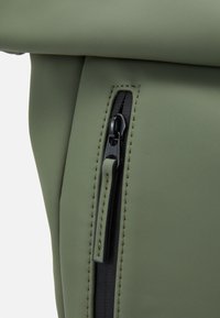 Grønn vanntett bag med matt tekstur, med en svart glidelås og kontrasterende sømmer. Designet er strømlinjeformet med minimalt med maskinvare.