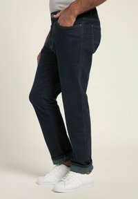 Granatowe dżinsy o slim fit, z klasycznym pięciopocketowym wzorem i subtelnymi detalami przeszycia, w połączeniu z białymi trampkami.