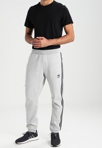 Svart kortärmad t-shirt i kombination med grå träningsoverallbyxor med svarta sidostripes och en Adidas-logotyp. Bärs med svarta träningsskor.