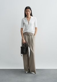 Top de malha branca com nervuras, colarinho e detalhe de amarração, combinado com calças largas bejes e uma pequena bolsa tecida preta.