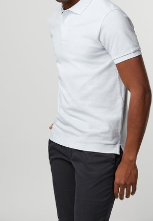 Polo shirt azzurro chiaro in tessuto di cotone testurizzato, con colletto, maniche corte e spacchi laterali per la ventilazione. Indossato con pantaloni scuri.