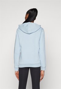 Ljusblå hoodie med en mjuk textur, som har en bred huva, ribbade ärmslut och en figursydd nederkant. Bärs tillsammans med svarta leggings.