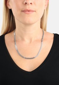 Collana in argento con maglie intrecciate, design piatto e finitura lucida, indossata sopra una maglietta nera a V.