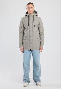 Light gray waterproof jacket with a hood, black drawstrings, snap buttons, and side pockets, paired with light blue wide-leg jeans.