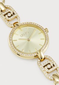 Gold stainless steel watch features a round face with a light green dial and crystal accents on bezel and bracelet links.