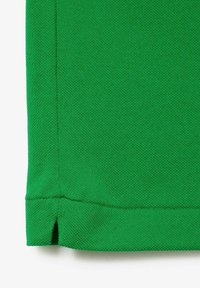 Tissu en coton vert avec une surface texturée. Doté d'un ourlet droit et de petites fentes latérales en bas.