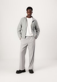 Lichtgrijze zip-up jack, witte t-shirt, grijze relaxte broek en zwarte chunky schoenen. Soepele stof, op maat gemaakte pasvorm, minimalistisch ontwerp.