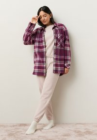 Camicia di flanella a quadri viola con chiusura con bottoni sopra un top aderente rosa chiaro e pantaloni jogger abbinati; tessuto morbido e dalla texture accogliente; calzini bianchi.