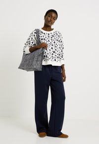 Sudadera blanca con estampado de leopardo en negro y azul marino, combinada con pantalones de pierna ancha en azul marino y un bolso de textura gris. Zapatos marrones.