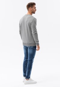Grijze sweatshirt gemaakt van gestructureerde stof, ronde halslijn, geribbelde manchetten, gecombineerd met blauwe spijkerbroek en witte sneakers. Achteraanzicht getoond.