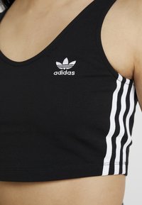 Černý sportovní crop top s kulatým výstřihem, se bílým vyšívaným logem Adidas a třemi bílými pruhy na straně.