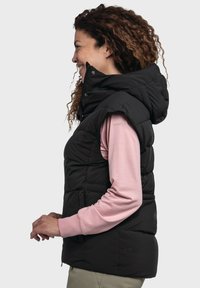 Schwarze Steppweste mit hohem Kragen und Kapuze, ausgestattet mit seitlichen Taschen und gestepptem Design. Getragen über einem hellrosa Langarm-Oberteil.